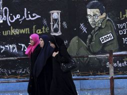 Jóvenes palestinas pasan ante un muro con una imagen del soldado israelí Gilad Shalit, en el campo de refugiados de Yabalia. EFE  /