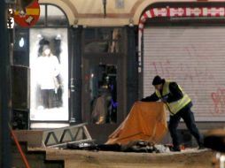Un policía tapa con una manta el cadáver del fallecido tras estallar dos coches en la calle Drottning de Estocolmo. EFE  /