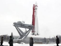Transeúntes caminan en Rusia frente a un modelo del primer cohete que voló al espacio exterior. EFE  /
