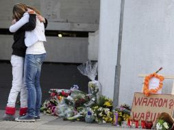 Dos mujeres se dan el pésame cerca de un mensaje que dice “¿por qué?”. AP  /