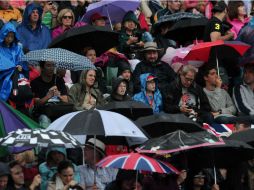 La gente espera la reanudación del partido, cubriéndose de la lluvia. AFP  /