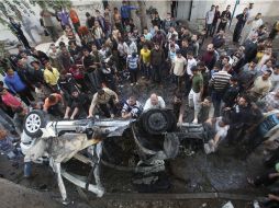 Ciudadanos palestinos se reúnen junto a un auto destruido por los bombardeos. REUTERS  /