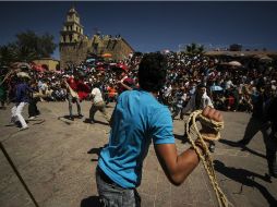 Adentro del círculo, hombres ataviados con capas rojas y verdes, se golpean con cuerdas.  /