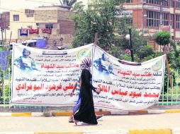 Personas pasan delante de carteles alusivos a Mahmud Abbas, activista chií iraquí asesinado en Siria. AP /