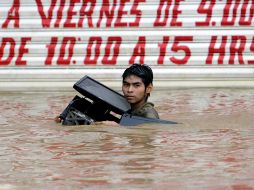 Un joven carga una computadora mientras se abre paso entre las inundaciones. AFP /