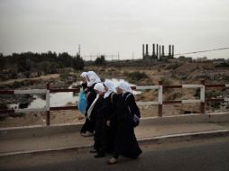 Unas escolares palestinas cruzan un puente en el centro de la Franja de Gaza, con la silueta de la central eléctrica al fondo. AFP /