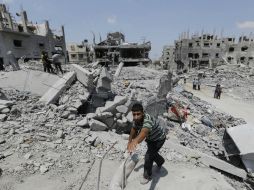 Palestinos caminan en los restos de viviendas destruidas por los bombardeos israelíes. AP /