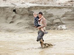 Hombre carga a un niño para atravesar una carretera, inundada por las lluvias que el metéoro causa en California. AP  J. Calderón  /