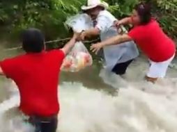 José Pablo Valadez, en medio de la fuerte corriente del arroyo, y sujeto a una cuerda, reparte ayuda a damnificados. YOUTUBE / Roberto Aguilar