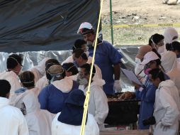 Los auxiliares forenses contribuyen a desarticular el fémur de cada cuerpo para fraccionarlo en cuatro partes. AFP / J. Villamil
