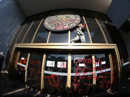 Uno de los encapuchados subió a la entrada y rayó el escudo de México con la palabra 'asesino'. EL INFORMADOR / R. Tamayo