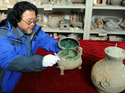 Un arqueólogo muestra la peculiar sopa; se pueden apreciar los huesos y el caldo, verdes por el proceso de oxidación de la vasija. ESPECIAL /