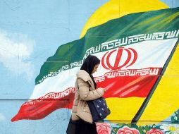 Una mujer revisa su celular mientras pasa por una imagen de la bandera de Irán conmemorativa del primer aniversario del acuerdo. EFE / A. Taherkenareh