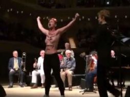 Una mujer con el torso desnudo y frases escritas en negro sobre la piel sube al escenario y grita con los brazos en alto. FACEBOOK / FEMEN