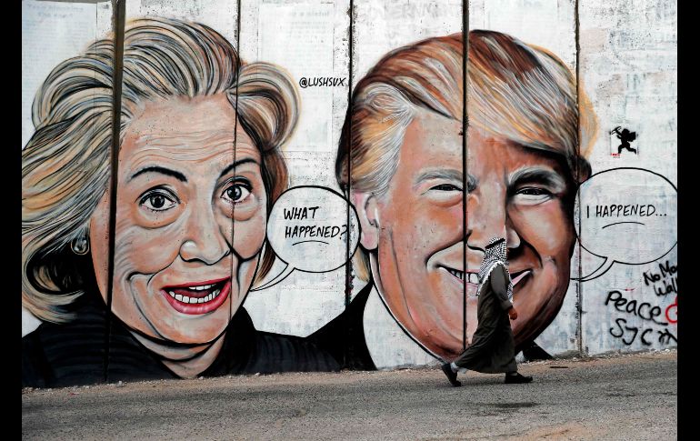 Un palestino pasa junto a un nuevo grafiti que muetra al presidente de Estados Unidos, Donald Trump, y la candidata presidencial Hillary Clinton en el controversial muro de israelí en Belén, que la separa de Jerusalén. AFP/T. Coex