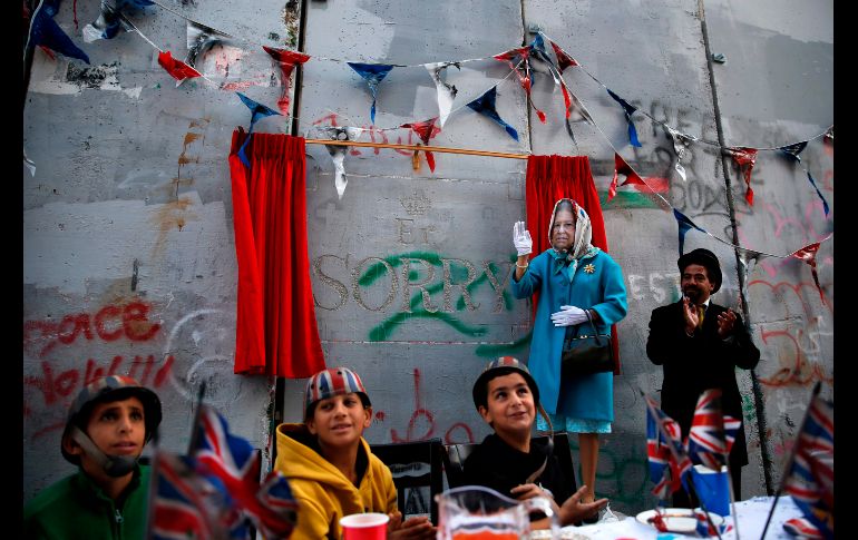 Un actor disfrazado de la reina Isabel y palestinos refugiados asisten a una ceremonia en Belén, Cisjordania, organizada por el artista británico Banksy como una 