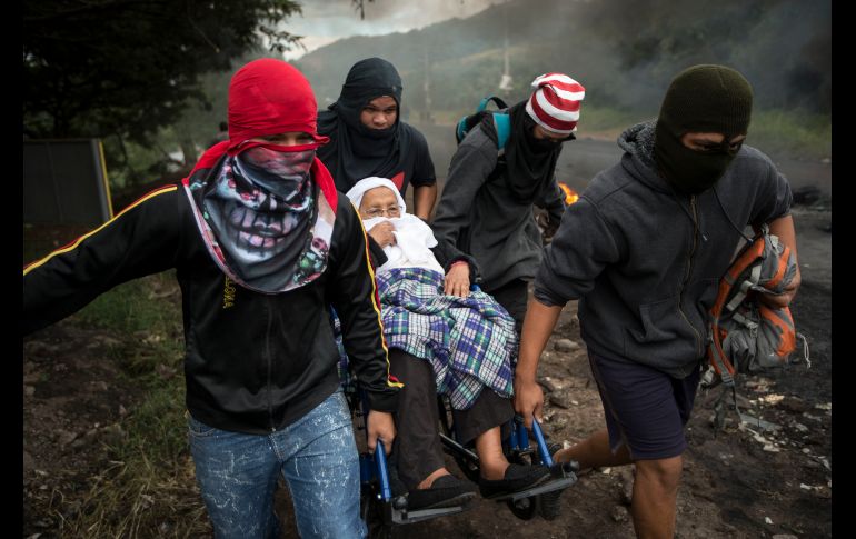 Opositores al gobierno ayudan a una mujer a pasar una barricada encendida durante un bloqueo en  Tegucigalpa, Honduras, realizado tras unas cuestionadas elecciones presidenciales. AP/M. Castillo