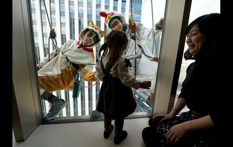 Limpiadores de ventanas disfrazados saludan a una niña en el distrito de compras y negocios de Yaesu, en Tokio, Japón. AP/S. Kambayashi