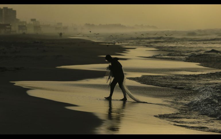 Un palestino camina con una red en la playa de la Ciudad de Gaza, en Territorios Palestinos. AFP/M. Hams