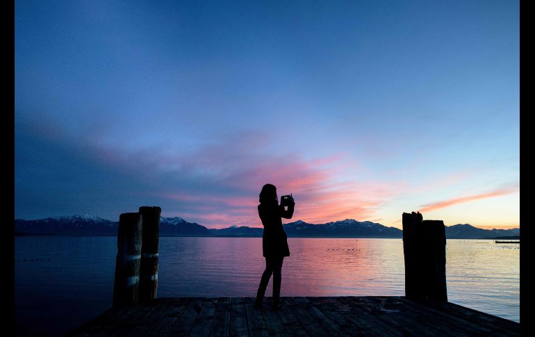 Una joven toma fotos del atardecer desde un embarcadero en el lago Chiemsee, en la población alemana de Seebruck. AFP/DPA/M. Balk