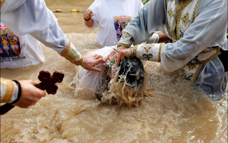 Un sacerdote cristiano ortodoxo bautiza a un peregrino en aguas lodosas del río Jordan, en el marco de las celebraciones de la Epifanía en Qasr al-Yahud, cerca de la ciudad cisjordana de Jericó. AFP/M. Kahana