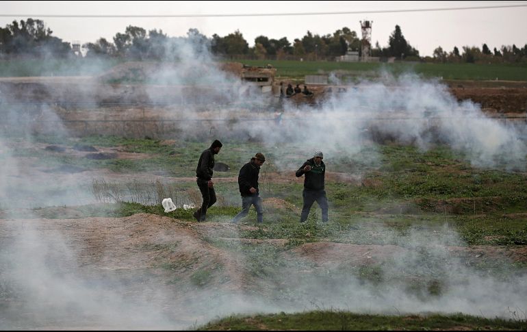 Manifestantes palestinos tratan de protegerse de unas granadas de humo durante enfrentamientos con las tropas israelíes en la Franja de Gaza. EFE/ M. Saber