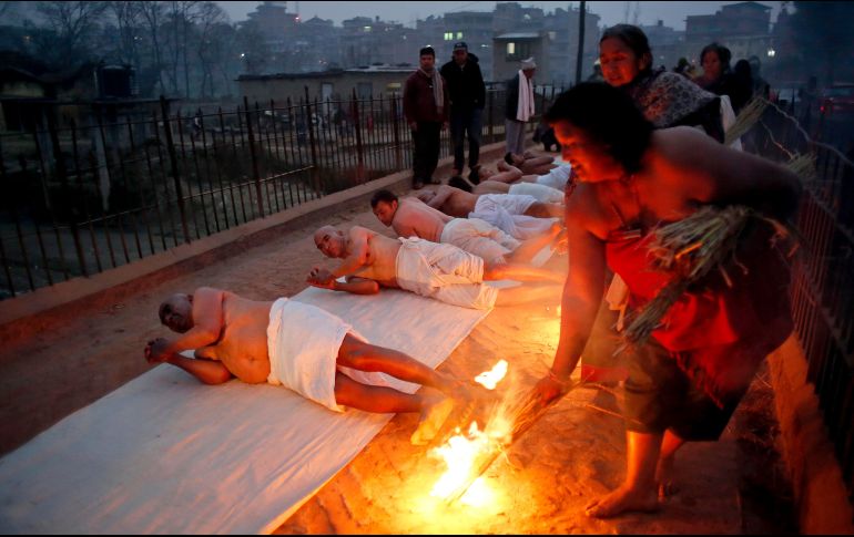 Devotos hindúes ruedan sobre el piso a las orillas del río Hanumante en Bhaktapur, Nepal, en el último día del festival 
