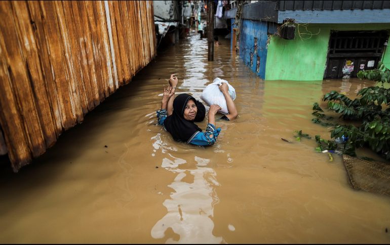 Una mujer y un niño intentan desplazarse, con el agua casi cubriéndolos por completo. EFE/M. Irham