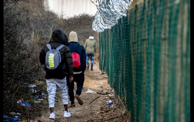 Migrantes caminan junto a una reja en el área de la terminal de transbordadores en Calais, Francia. AFP/P. Huguen