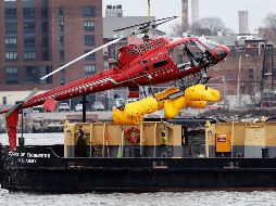 A helicopter is hoisted by crane from the East River onto a barge - A helicopter is hoisted by crane from the East River onto a barge, Monday, March 12, 2018, in New York. The pilot was able to escape the Sunday night crash after the aircraft flipped upside down in the water killing several passengers, officials said. (AP Photo/Mark Lennihan) APTOPIX NYC Helicopter Crash