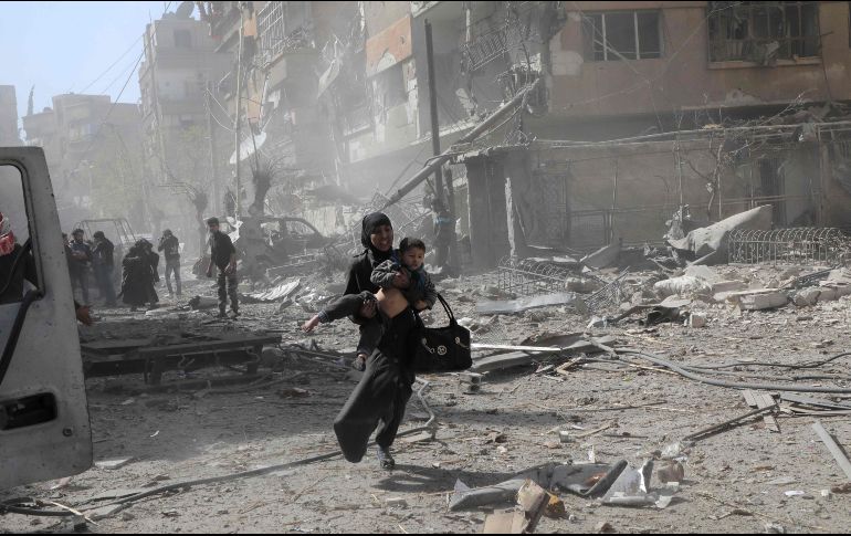 Una mujer con un niño huye de los bombardeos aéreos en Douma, Siria, en la región bajo control de los rebeldes al gobierno. AFP/H. Al.Ajweh