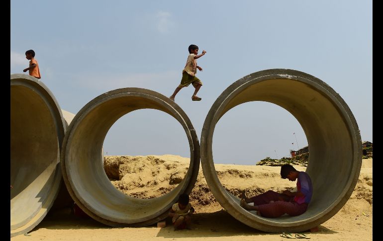 Un refugiado rohingya interactúa con su hijo mientras los niños corren sobre tuberías de aguas residuales en el campamento de refugiados de Kutupalong en Bangladesh. AFP / M. Uz Zaman