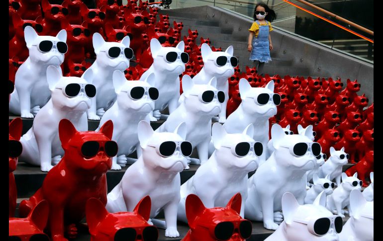 Una niña con un cubrebocas pasa junto a bocinas en forma de perros, desplegadas en un distrito comercial de Pekín. AP/N. Han Guan