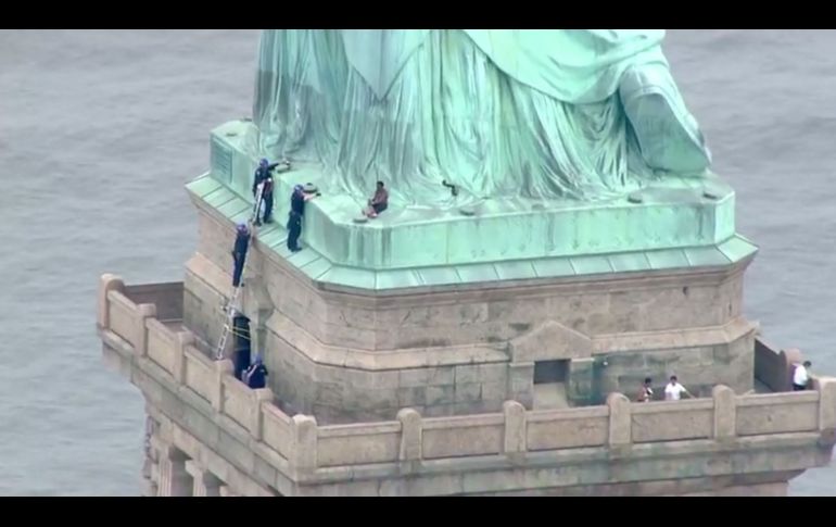 Policías hablan con una mujer que escaló la base de la Estatua de la Libertad en Nueva York. La isla en la que se encuentra el monumento tuvo que ser desalojada a raíz de la presencia de la mujer y tras el arresto de varias personas por colgar en el pedestal un letrero en el que se pide la eliminación del Servicio de Control de Inmigración y Aduanas. AFP/PIX11 News