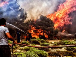 Bomberos intentan sofocar las llamas que se extienden por la costa ateniense. EFE/V. Psomas