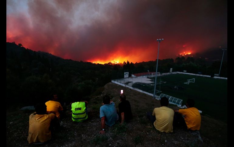 El incendio forestal continúa este domingo tras desatarse el mediodía del pasado viernes. Personas observan en la población de Brejo.