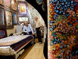 Dos hombres iraníes conversan dentro de su negocio de alfombras en el Gran Bazar de Teherán. La importación de estos productos se verá afectada con la medida. EFE/A. Taherkenareh