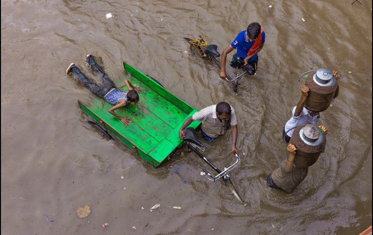 Lecheros y personas con bicis pasan por una calle inundada tras fuertes lluvias en Allahabad, India. AP/R. Kumar Singh