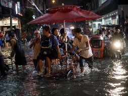 Un hombre traslada a bordo de un triciclo a varias personas a través de las calles inundadas. AFP/N. Celis
