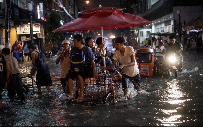 Un hombre traslada a bordo de un triciclo a varias personas a través de las calles inundadas. AFP/N. Celis