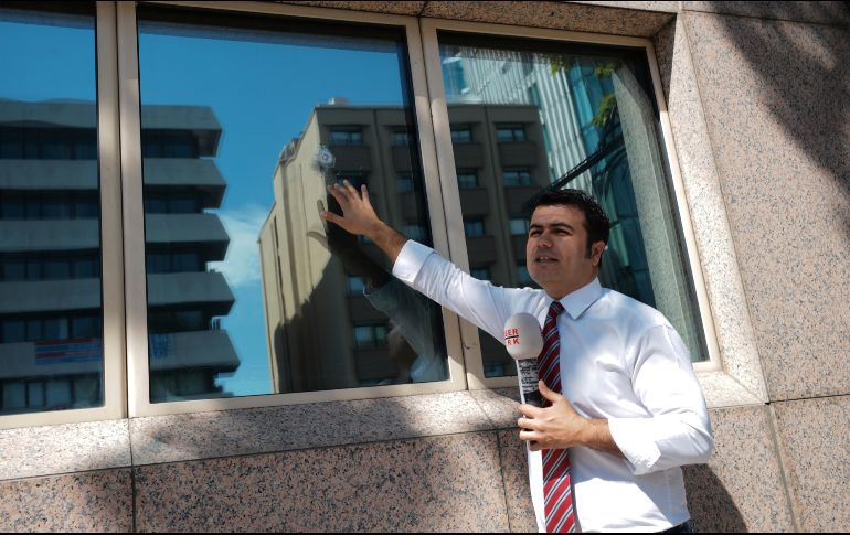 Un reportero, que realiza una transmisión en vivo, muestra el daño ocasionado por una bala en una de las ventanas de la sede diplomática estadounidense. AP / B. Ozbilici