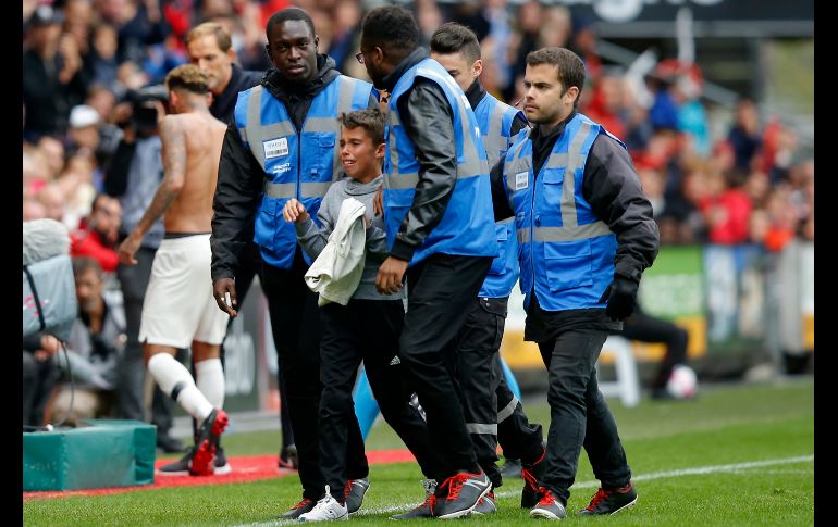Guardias escoltan a un niño que sostiene una playera que le dio Neymar, del PSG, al final del partido de la Liga francesa ante Rennes, en el estadio de Rennes, Francia. El niño se abrió paso en la cancha para abrazar al astro brasileño. AP/M. Euler
