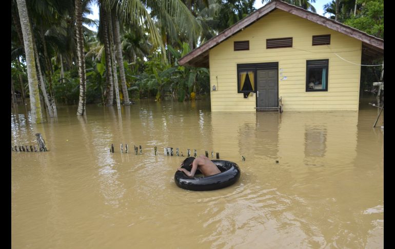Un niño juega con un tubo de un auto en una zona inundada en Teunom, Indonesia, tras fuertes lluvias. AFP/C. Mahyuddin