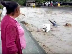 Algunas personas lanzan cuerdas al hombre, quien es arrastrado por la corriente de agua junto a su motocicleta. Los primeros intentos no tienen éxito. YOUTUBE / Alekina Deniss
