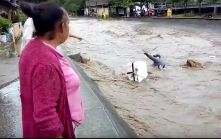 Algunas personas lanzan cuerdas al hombre, quien es arrastrado por la corriente de agua junto a su motocicleta. Los primeros intentos no tienen éxito. YOUTUBE / Alekina Deniss