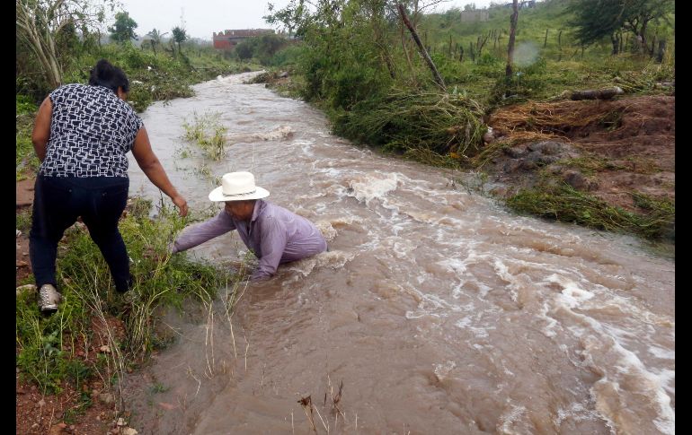Un hombre cruza un canal crecido en Escuinapa.