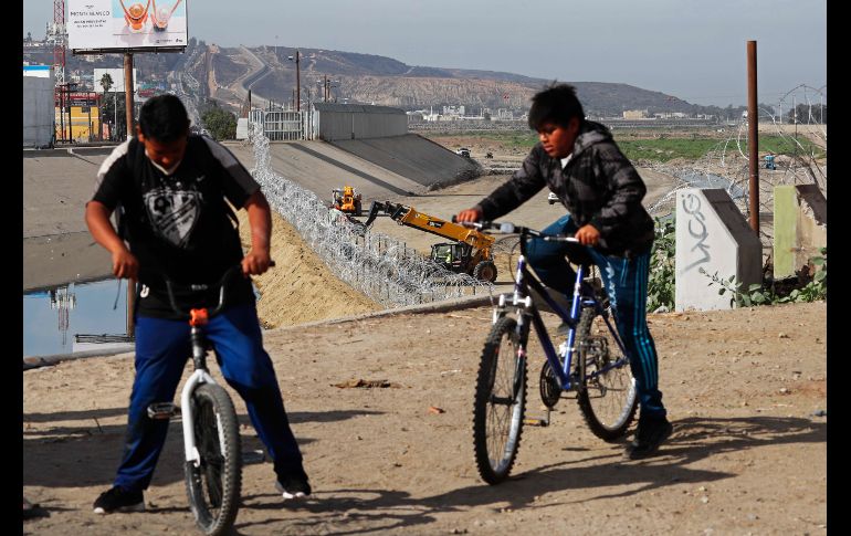 Jóvenes andan en bici en Tijuana, Baja California, mientras trabajadores colocan alambre de púas en la frontera de San Ysidro, Estados Unidos. P/M. Ugarte