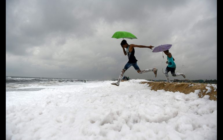 Jóvenes saltan sobre agua espumosa, provocada por contaminantes, en una playa en Chennai, India. AFP/A. Sankar