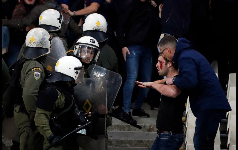 Un aficionado de Ajax detiene a otro, herido, luego de enfrentamientos con policías en un partido de la Liga de Campeones entre AEK y Ajax en el estadio OAKA en Atenas, Grecia. Los altercados causaron 11 heridos. AP/T. Stavrakis