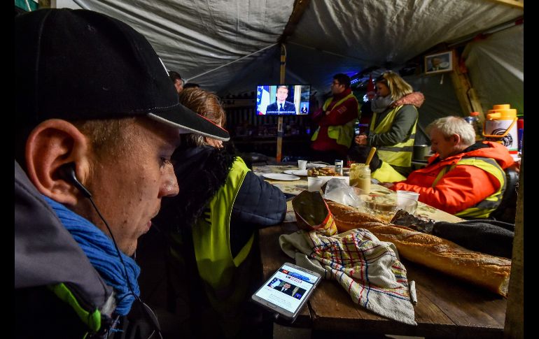Franceses en chalecos amarillos miran la transmisión del mensaje del presidente Emmanuel Macron en una tienda de campaña en una carretera de Montabon, Francia. Macron anunció el lunes una serie de medidas para apaciguar las protestas de los 